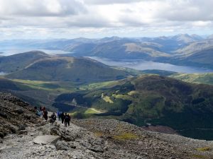 A landscape view looking down from Ben Nevis towards the lochs in the distance and with the stony path in the foreground