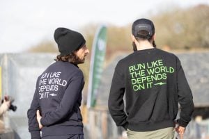 Two volunteers standing with their backs to the camera wear hoodies with the words 'run like the world depends on it' written on the back