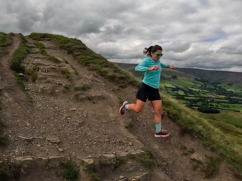 A woman running down a worn path in the hills of the Peak District