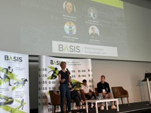 A woman holding a microphone onstage as part of a panel discussion on sustainable sport