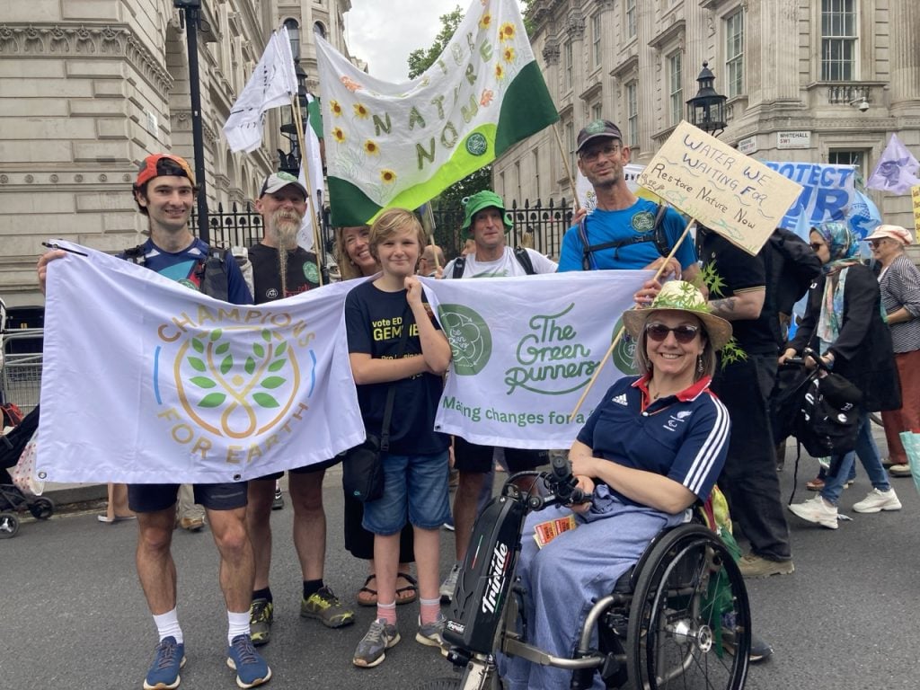 A group of seven people holding banners reading 'Champions for Earth', 'The Green Runners' and 'Restore nature now' standing outside Downing Street in London. One is in a wheelchair wearing a Team GB top, the others are standing wearing sports clothes and sporting green runner badges.