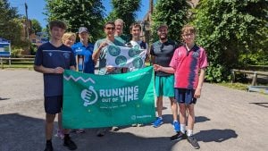 A group of people in a car park on a sunny day holding a Climate Relay banner. They are also holding a Green Runners banner