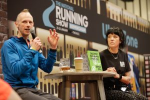 Damian Hall, left, and Allie Bailey, right, in conversation sitting at a table at the National Running Show 2024.