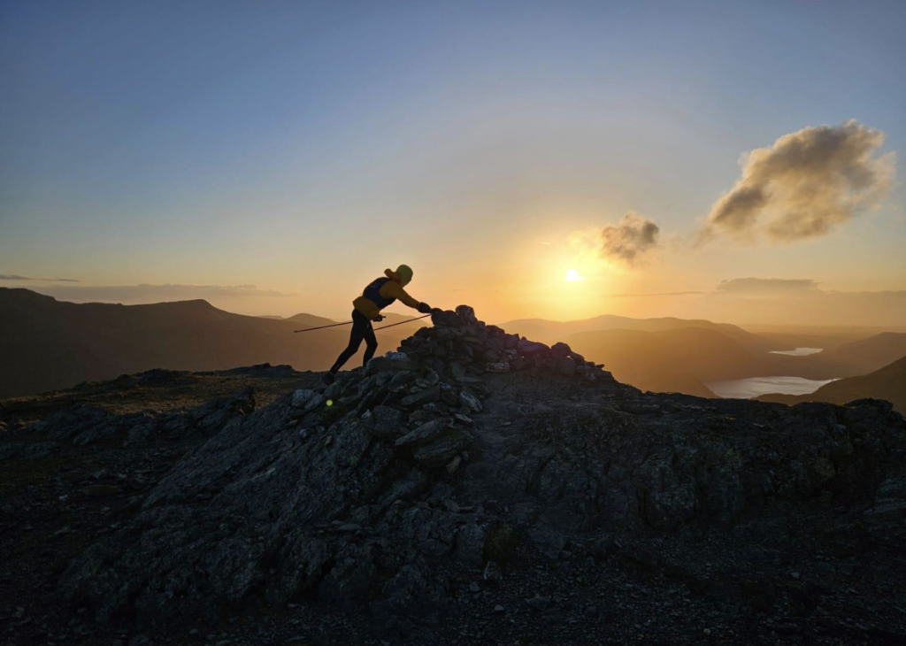 A sunset image of a man touching the summit of a mountain. 