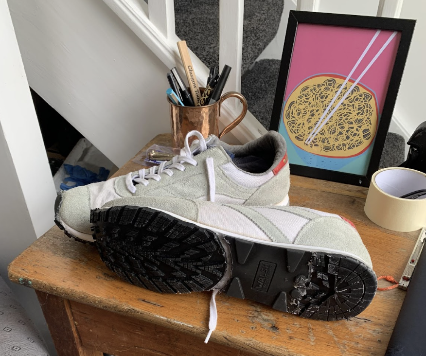 A photo of a pair of repaired shoes on a table. They are pale green in colour with white laces and a grippy outsole.