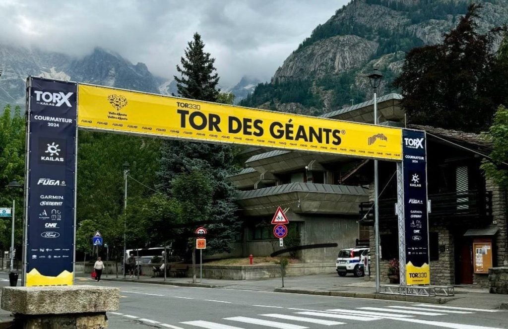 A large archway astride a road. The arch is yellow and blue with TOR DES GEANTS written across it and the Ford brand featured amongst other sponsors.